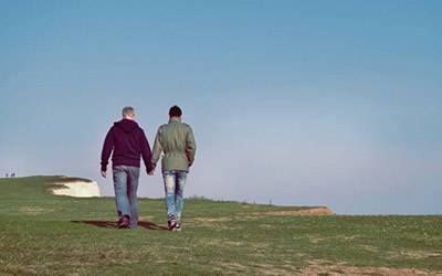 male couple holding hands on a hill.