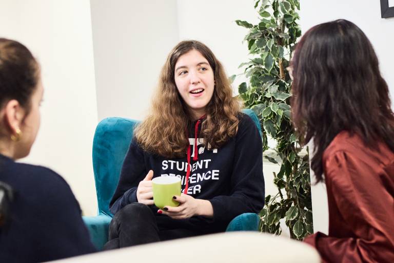 A Student Residence Adviser sitting and talking with two students in a common room in a student hall