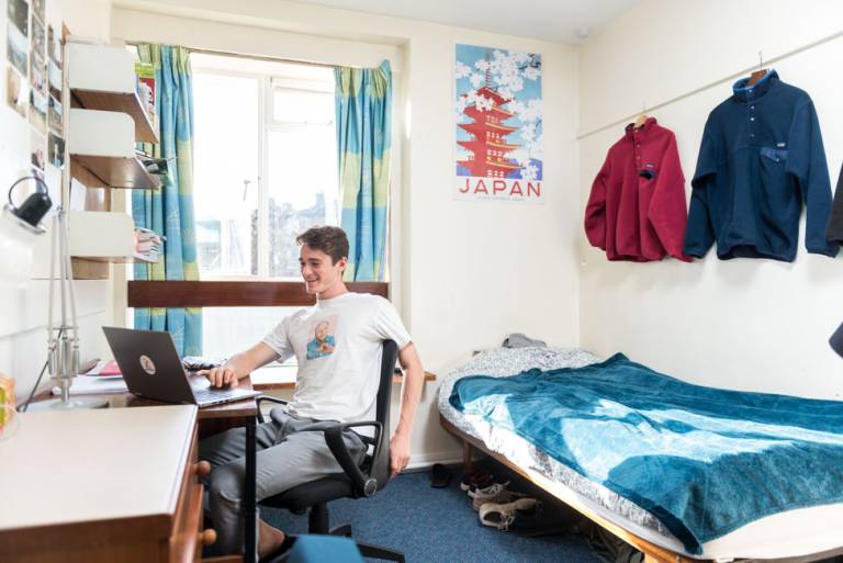 Male student smiling at laptop in his room