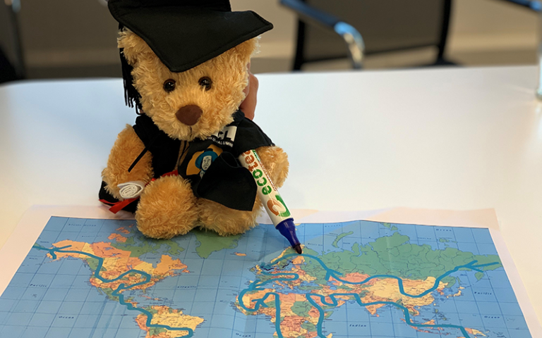 A teddy bear ('Jeremy Beartham') posed to look like it is drawing on a map of the world