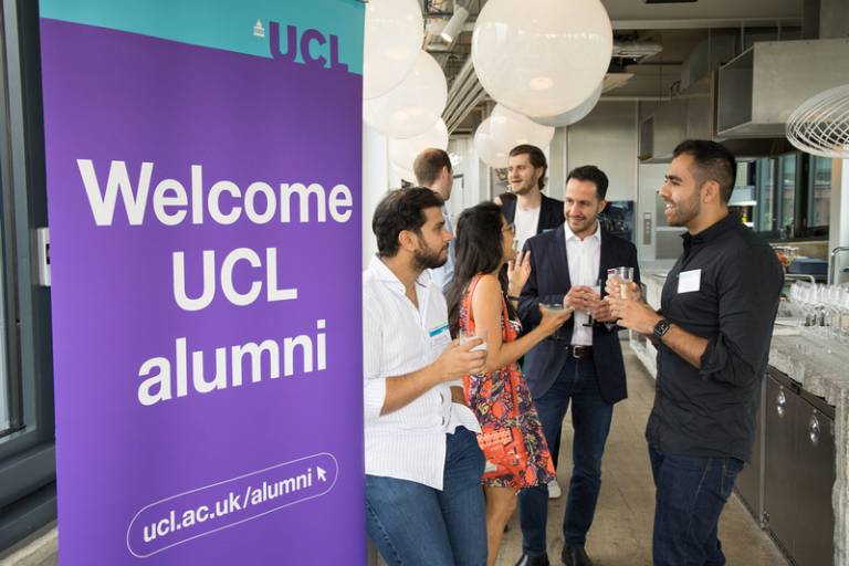 Photo of a welcome UCL alumni banner with four alumni talking to each other