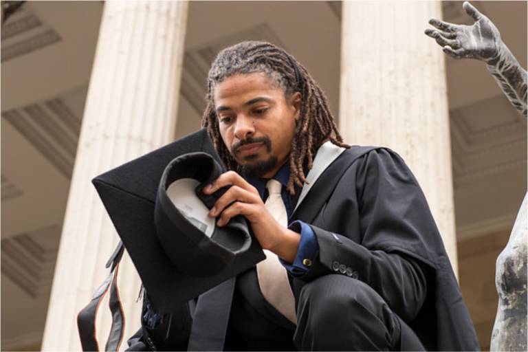 Photograph of a black male student, sitting on the steps of the UCL Portico on graduation day