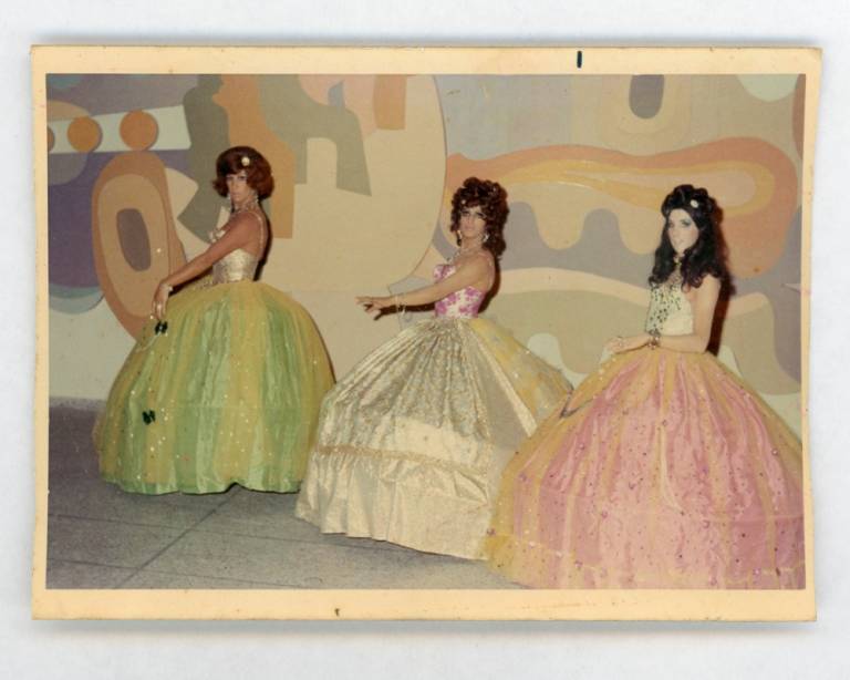 Photograph of three persons, self-identifying as transwomen, dressed in gala gowns; taking part in what appears to be a choreographed tableau