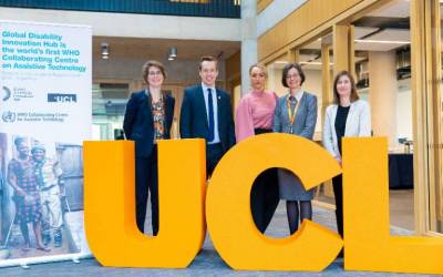 A group of staff from the UCL GDI Hub stand, with UK Minister for Disabled People Tom Pursglove, next to some large orange letters that spell out 'UCL'.