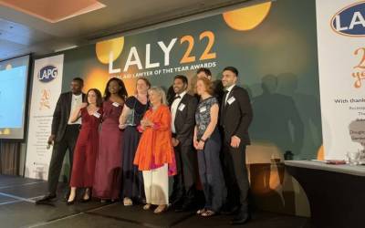 UCL ILAC winning a Legal Aid Lawyer of the Year award in 2022. The team of nine people are standing on stage smiling, with one of them holding the award.