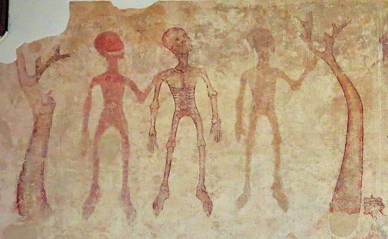 A painting of three red skeletal figures between two trees on a Medieval church wall. One holds up a hand in greeting.