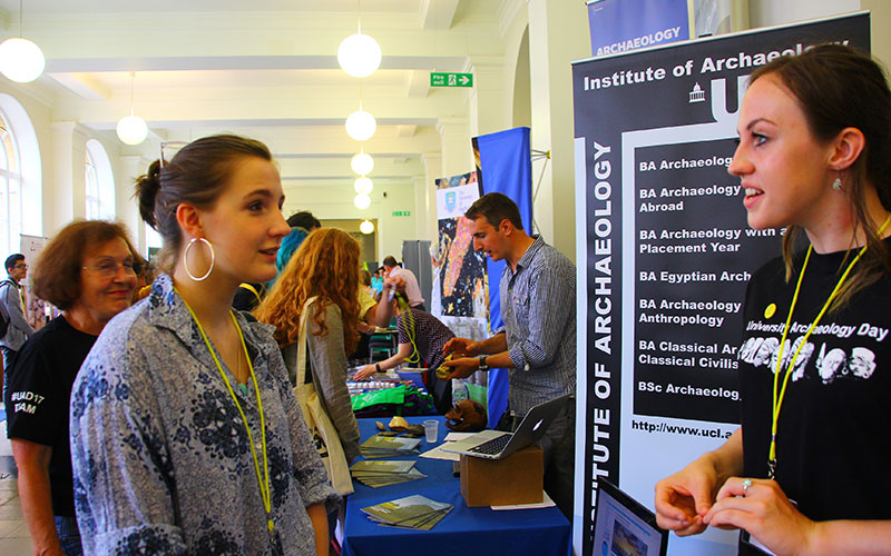 People at an academic exhibition/open day with banners in the background and tables of merchandise