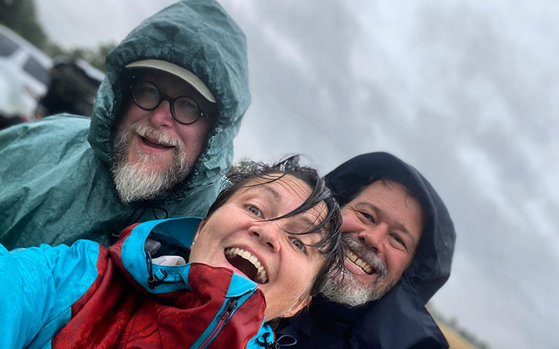 Close up image of three people in the rain smiling at the camera