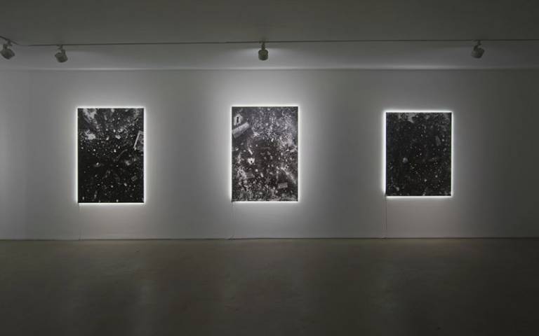A darkened gallery/display space with three rectangular displays and spot lighting overhead