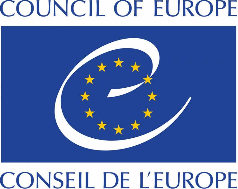 Blue rectangle with a white swirl in the centre and a circle of yellow stars. Blue text top and bottom in English and French. 