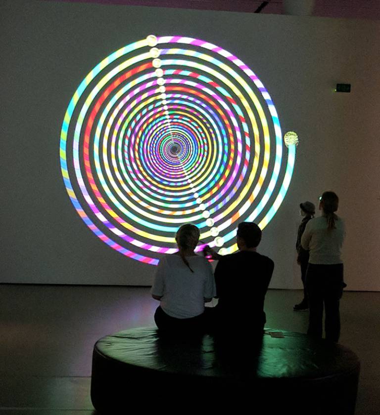 Four people in a darkened museum space looking at a colourful spiral display