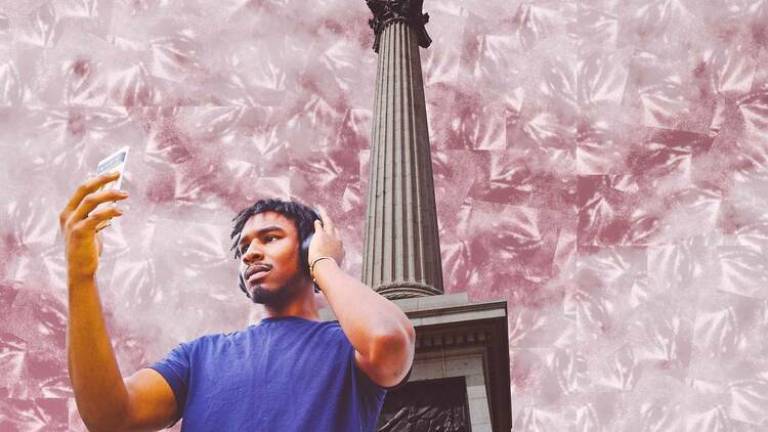 A man of colour in a blue t-shirt, wearing earphones and holding up a smart phone, standing in front of a stone column, with an abstract coloured sky (pink/silver) overhead