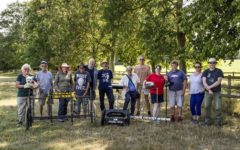 Group of 12 people (a community group) standing in a field with some surveying equipment 