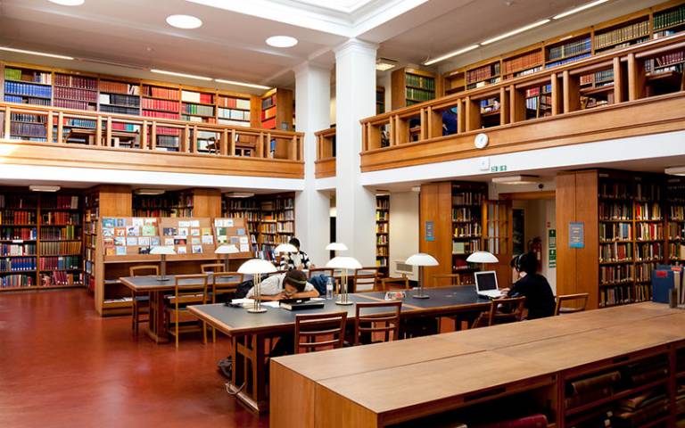 Students sitting in a library space with bookshelves surrounding the tables they are working at