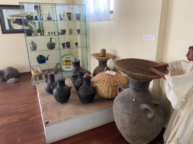 A display in a room of different types of pottery (various colours/sizes) some in a glass case, others on a raised dais 