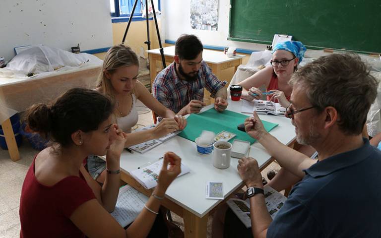 Five people sitting around a table, a bearded man in a green top teaching four students (3 female, 1 male)