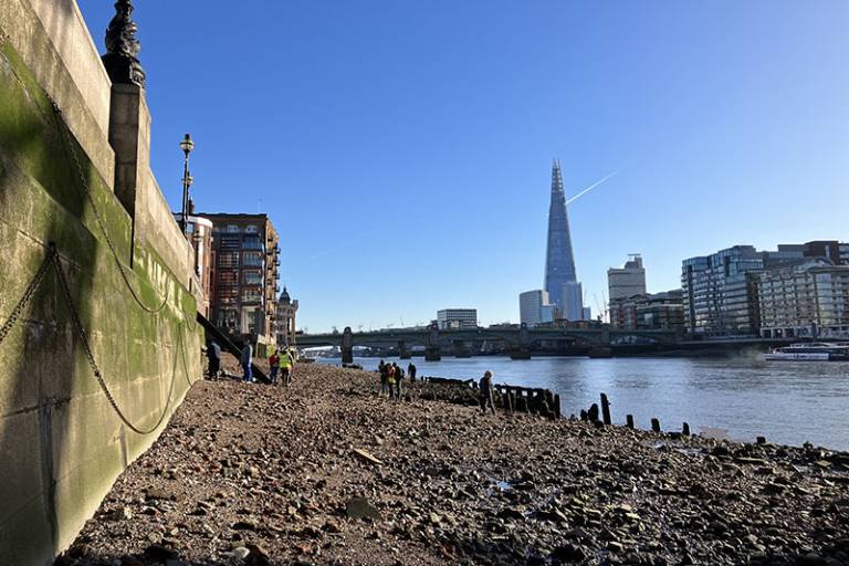 A sunny day in London with people in the distance standing on the Thames foreshore with wooden structures in the foreground