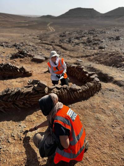 Two people in orange high-vis jackets excavating in the desert