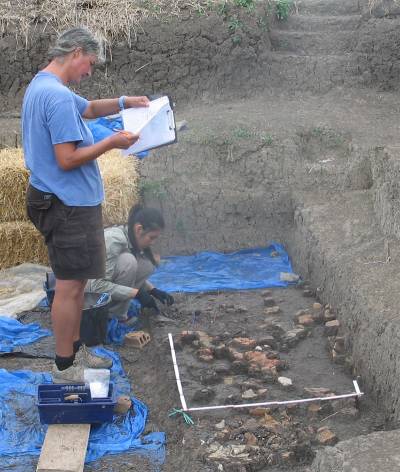 Two women, one standing, one crouching down, working on an archaeological excavation