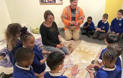 A man and a woman kneeling on the floor with a group of schoolchildren producing hand painting artwork