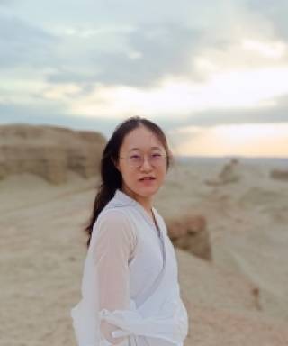 Picture of Shiyue Yang who is looking straight at the camera. She is standing on the edge of some barren mountains