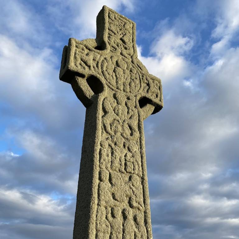 a stone monument in the shape of a cross against a cloudy sky
