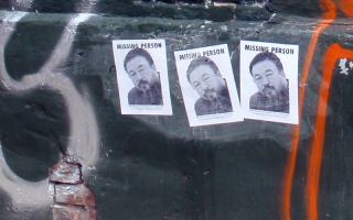 three black and white missing person posters of a man against a black wall that's been spray painted