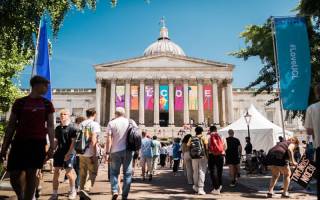 An image of main UCL Bloomsbury campus building with colourful banners hanging down spelling the word welcome to all the new students. Many students are pictured walking in front of it.