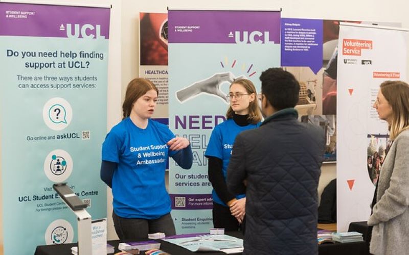 Two student ambassadors in blue tops speak to people about support at University College London at the 2023 Welcome Event