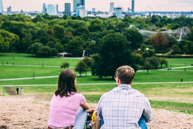 Two people sitting on Primrose Hill looking at the London skyline