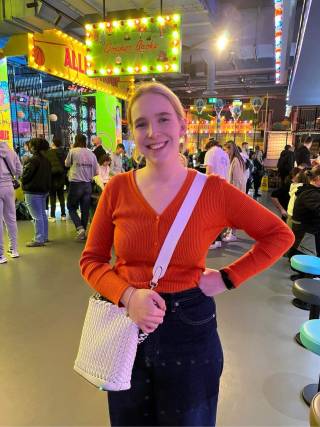 Jessica standing in an arcade. Red top and jeans with a white bag. 