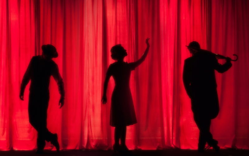 Image of 3 silhouettes against a red curtain