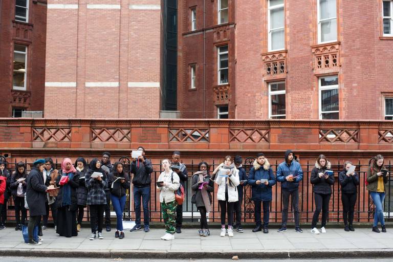A line of young people sketching in front of a red brick wall
