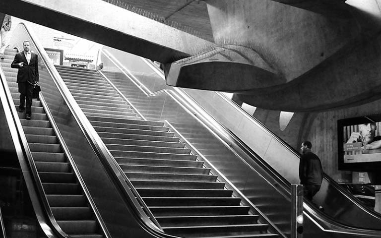 Black and white photograph of two men going up and down escalators in opposite directions