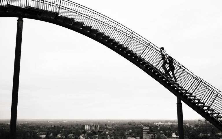 black and white photo of man walking over a curved bridge