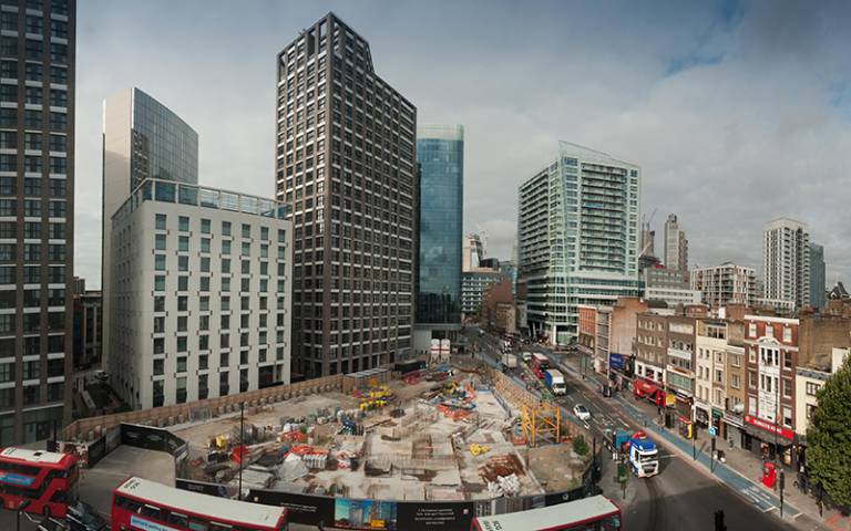Buses drive around a building site surrounded by tall buildings in Whitechapel