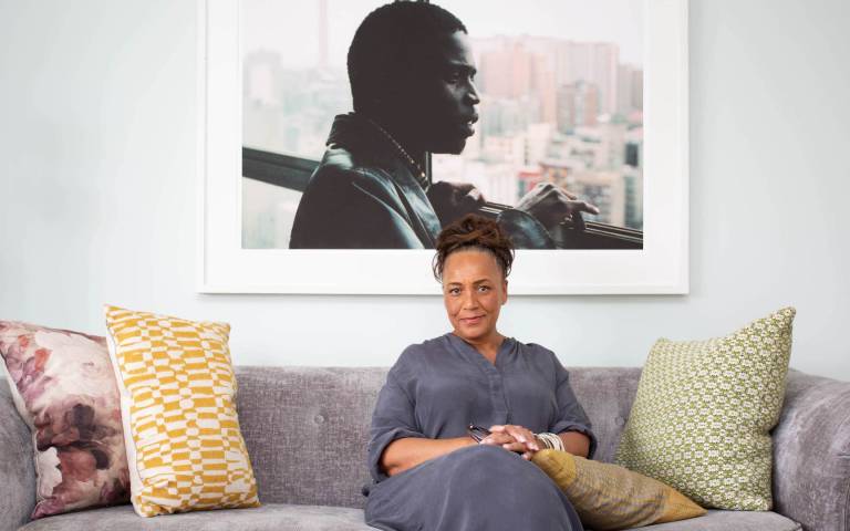 Image: Lesley Lokko seated on a sofa in front of a large portrait. Photo by Festus Jackson-Davis.