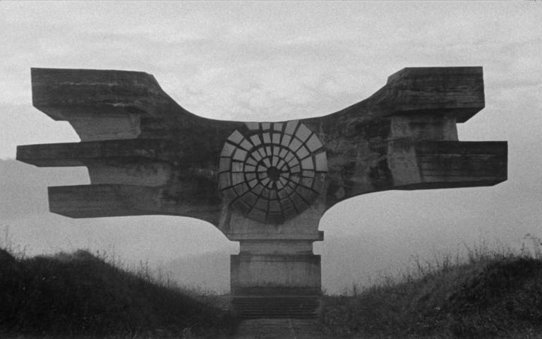 Misty black and white film still of a former Yugoslavian monument on top of a hill.
