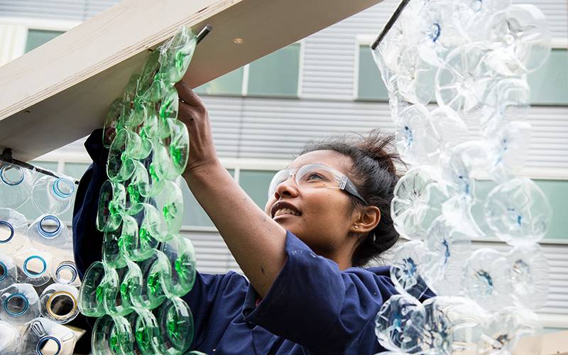A female student hangs an installation made of parts of plastic bottles 