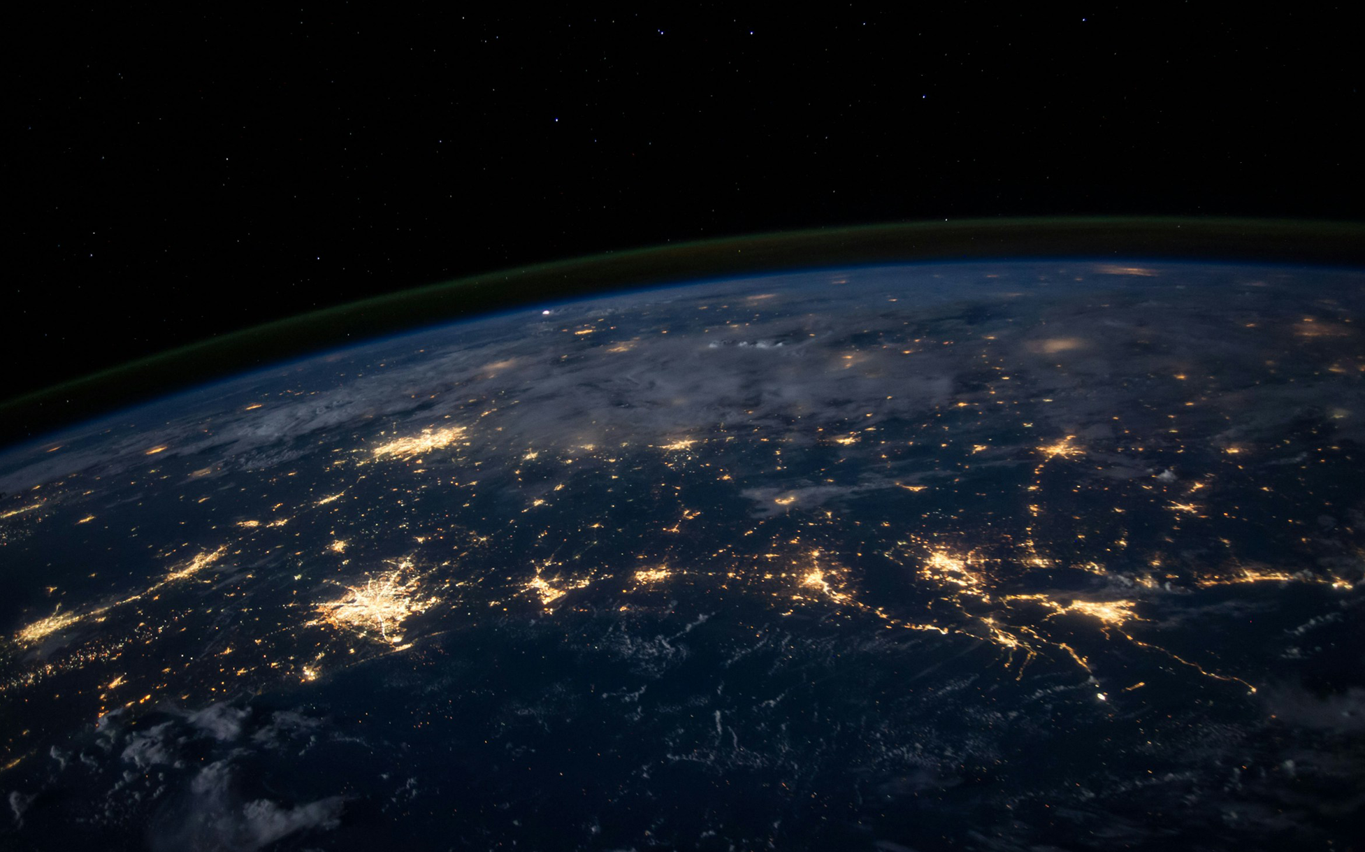 View of earth at night from space showing city lights, surrounded by darkness above.