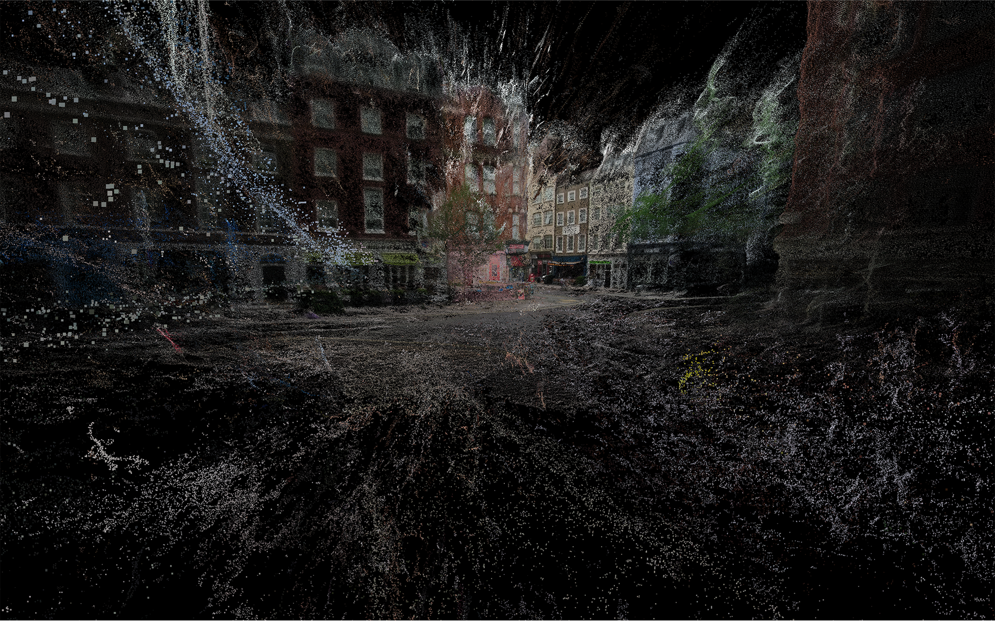 A London street view - rendered with the image formed of dust-like particles that are denser towards the centre of the image and less denser towards the edges. The street image contains a road junction and multiple shop fronts beneath red brick flats 