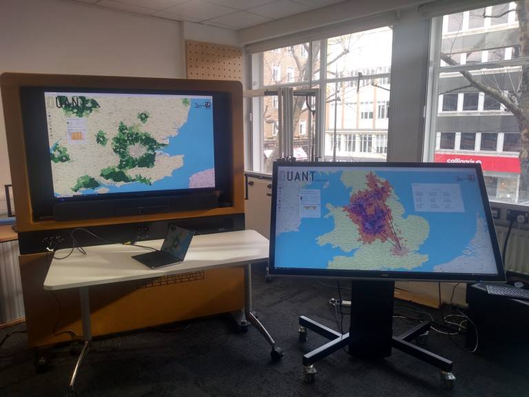 A laptop on a table alongside two screens displaying maps of the United Kingdom.