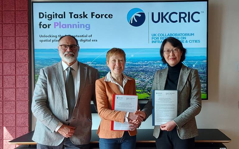 Professor Chris Rogers, Dr Joanne Leach, Dr Wei Yang standing in front of a PowerPoint slide displaying text "Digital Task Force for Planning and UKCRIC logo". Joanne and Wei are shaking hands. 