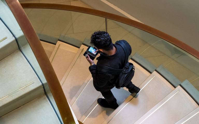 Student studying their phone as they walk down UCL's main library staircase. 