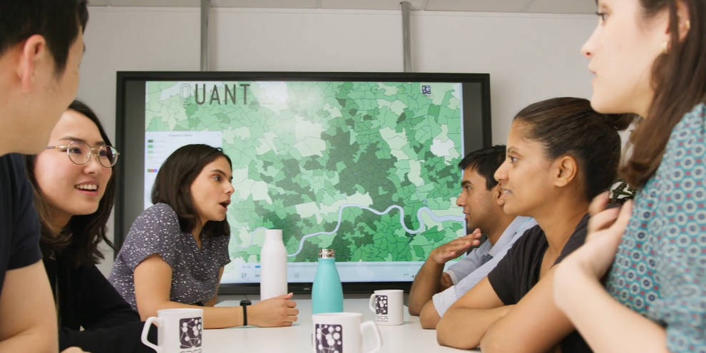 Group of students having a discussion around a table, with a computer screen with map of London