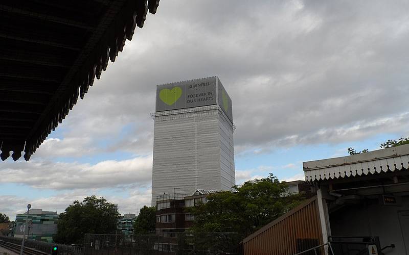 Grenfell Tower with banners at the top with heart symbol and the wording "Grenfell Forever In Our Hearts" in June 2018. The topping out of the protective sheeting and scaffolding took place in time for the 1-year anniversary of the Grenfell Tower Fire.