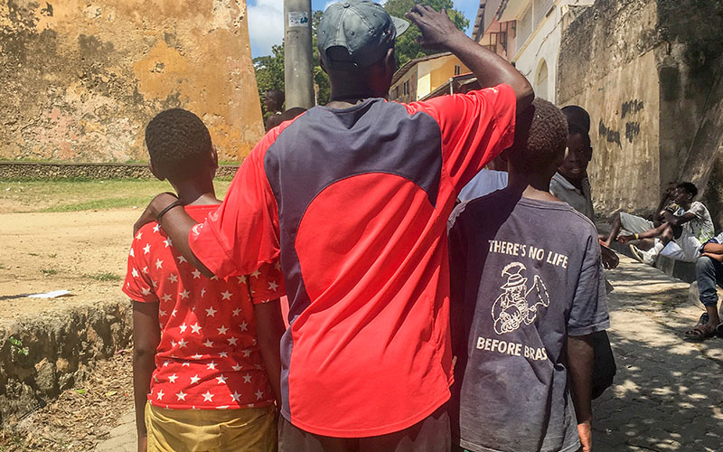 Image of a man standing facing away from the camera wearing a hat and red t shirt. Two children stand either side of him.  