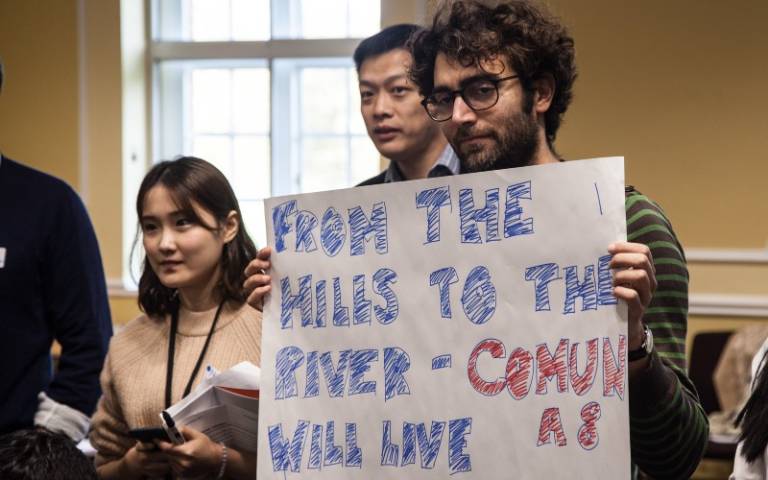 A student holds up a sign reading 'From the hills to the river - Comuna 8 will live'