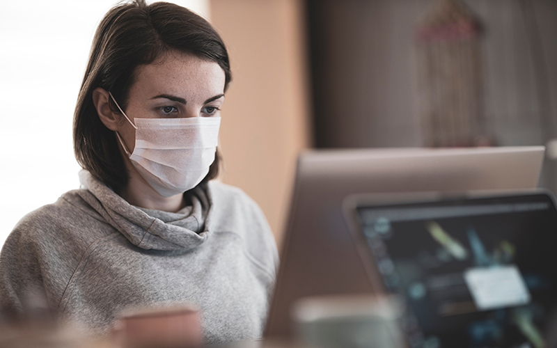 Photo of a woman using a computer wearing a face mask