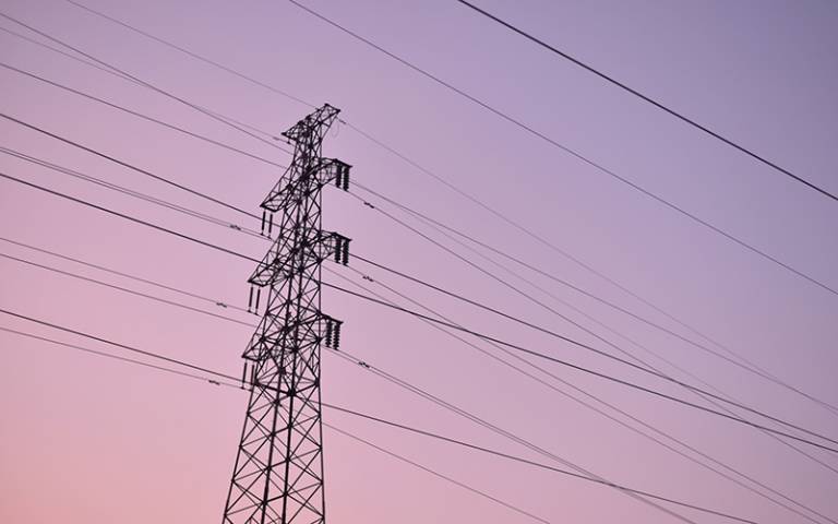 Photo of a pylon and cables against a pink sunset.